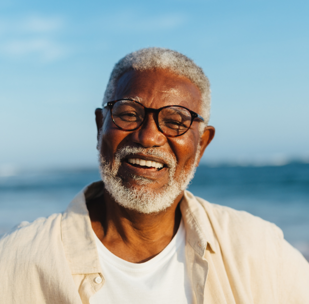 Senior man smiling at camera wearing glasses against ocean beach background