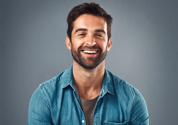 Smiling man in blue shirt against gray background, professional headshot for dental practice.