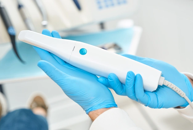Dentist in blue gloves holding intraoral camera in dental office setting.